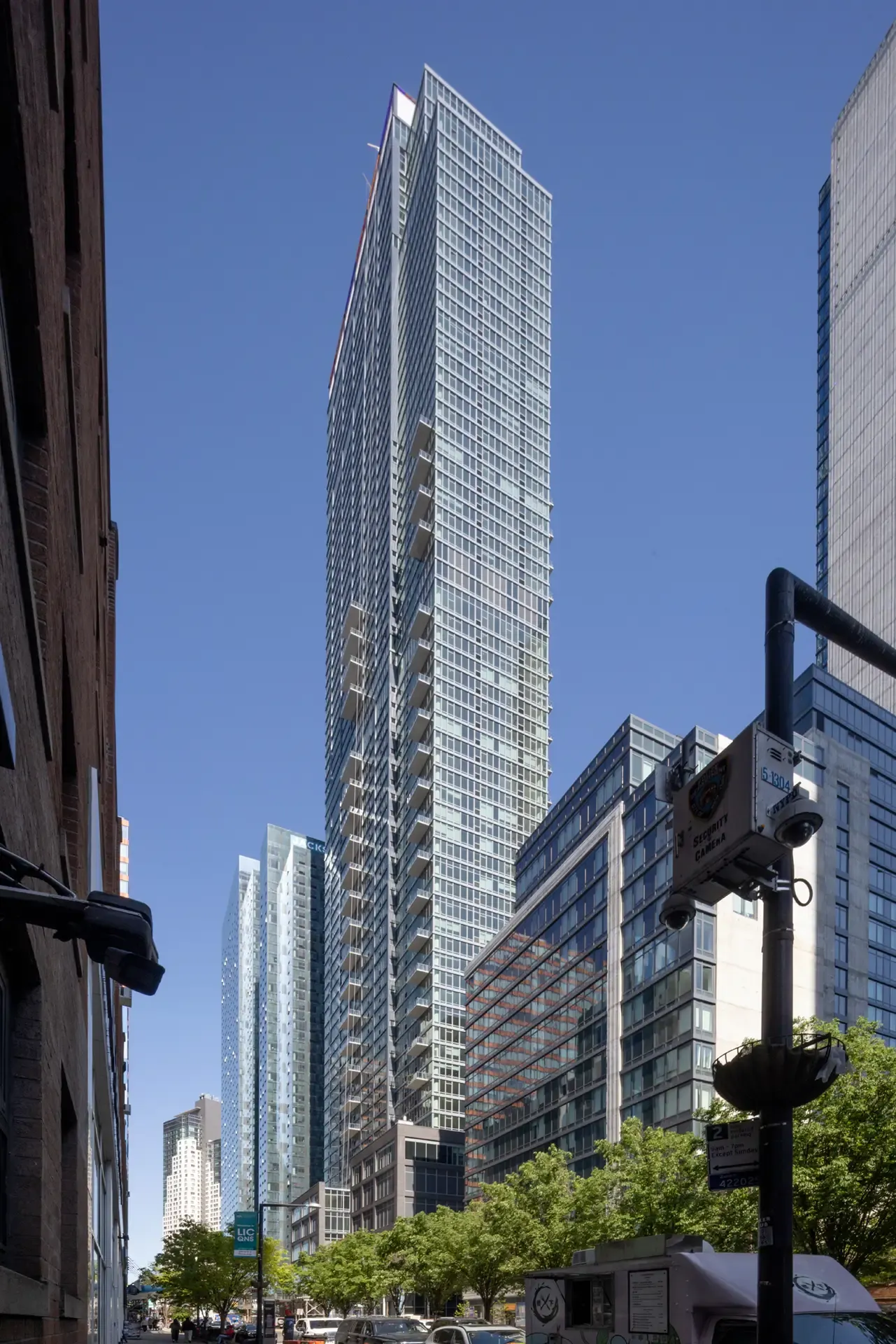 Full-height view of The Orchard residential tower with signage, parking structure and nearby buildings in Queens.