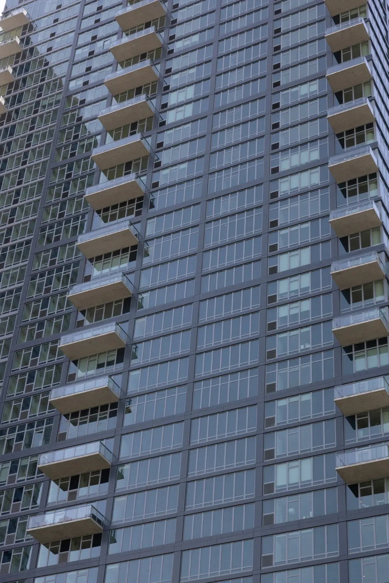 Close-up of The Orchard’s glass facade with stacked balconies and a regular window grid.