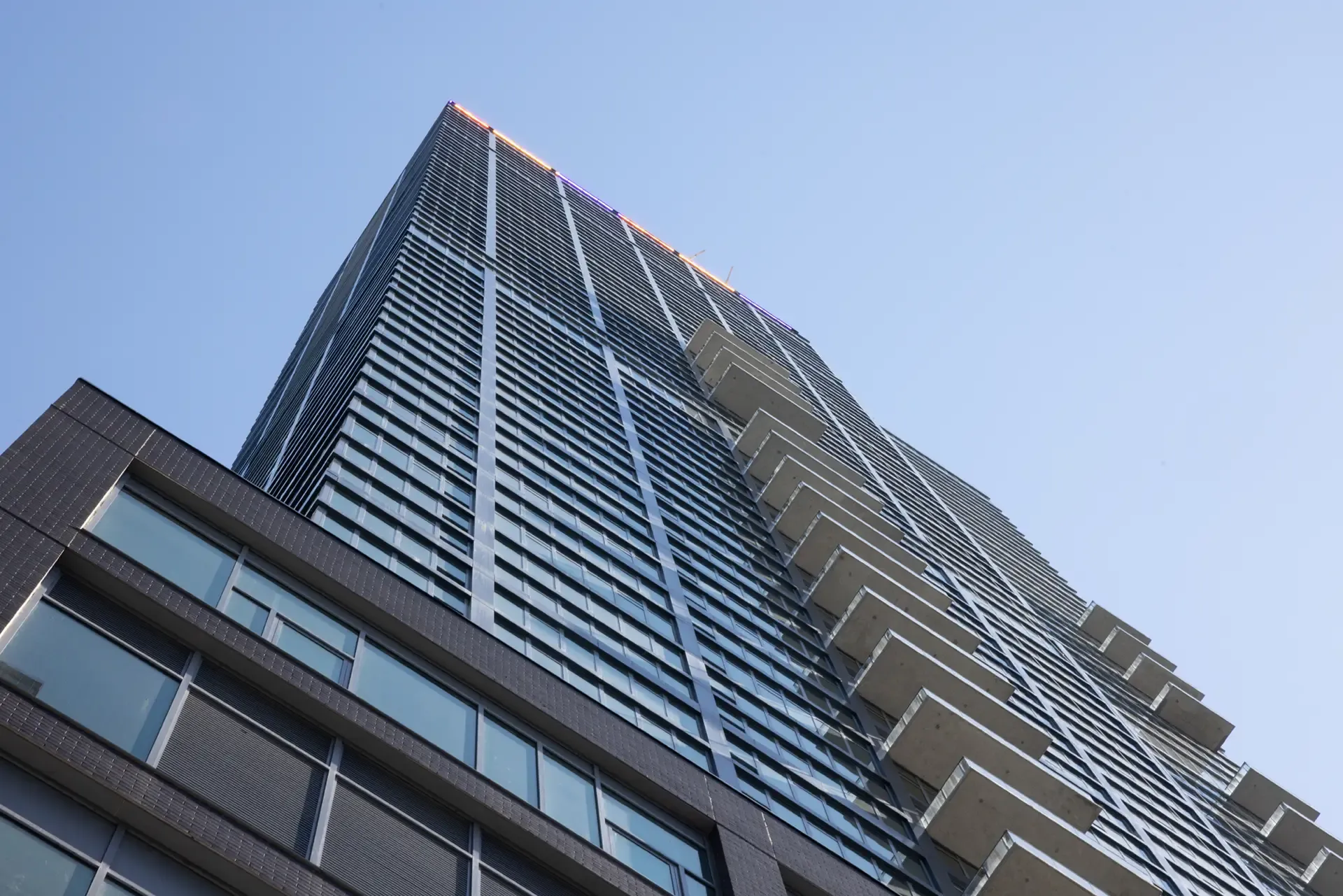 Low-angle view looking up at The Orchard’s tall glass facade and projecting balconies.